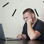 Male Student looking at a laptop. Clock in the background