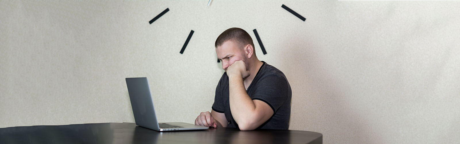 Man looking at a laptop under a clock