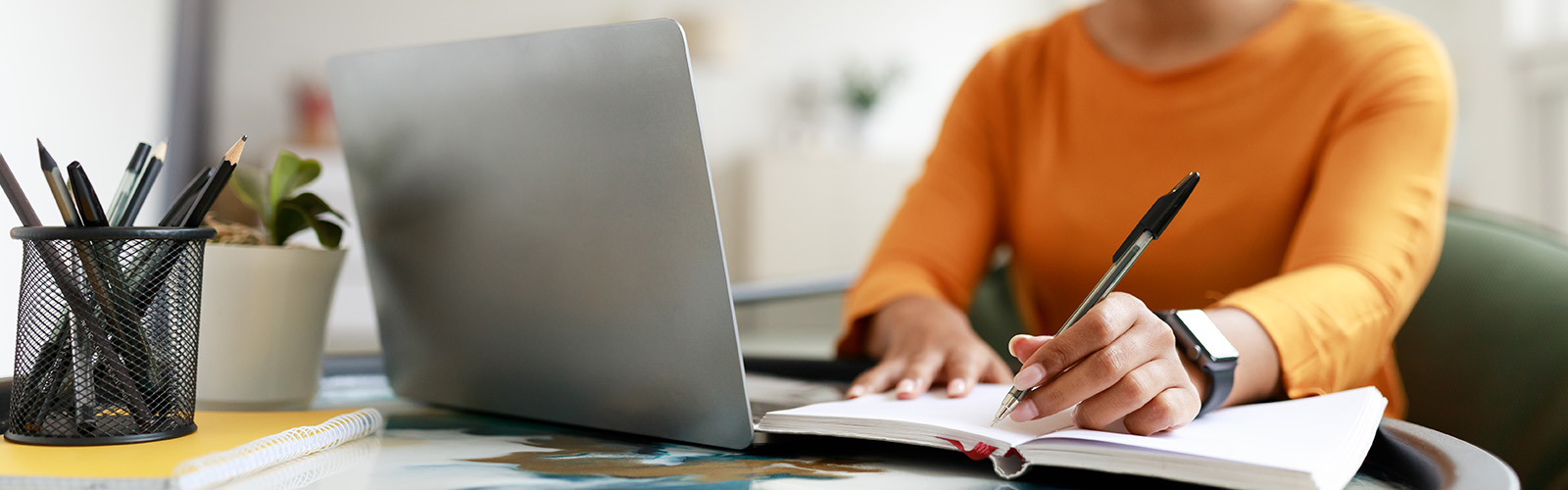 Woman sitting at desk, using computer and writing in notebook